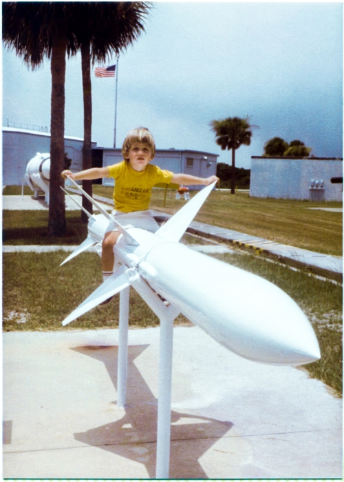Kai MacLaren sits atop the Sparrow air-to-air missile at the Air Force Space and Missile Museum, Cape Canaveral Air Force Station, Florida. Partially visible behind him, extending out of frame on the left, is the blockhouse where launches at Complex 26 were conducted and controlled, and between it and Kai, a Minuteman intercontinental ballistic missile can also be seen. To the right of Kai, ground level, extending from out of frame right, all the way to the blockhouse, a metal-covered cable trench which carries electrical power and instrumentation cables to the launch pad can also be seen. Photograph by James MacLaren. Kai MacLaren sits atop the Sparrow air-to-air missile at the Air Force Space and Missile Museum, Cape Canaveral Air Force Station, Florida. Partially visible behind him, extending out of frame on the left, is the blockhouse where launches at Complex 26 were conducted and controlled, and between it and Kai, a Minuteman intercontinental ballistic missile can also be seen. To the right of Kai, ground level, extending from out of frame right, all the way to the blockhouse, a metal-covered cable trench which carries electrical power and instrumentation cables to the launch pad can also be seen. Photograph by James MacLaren.